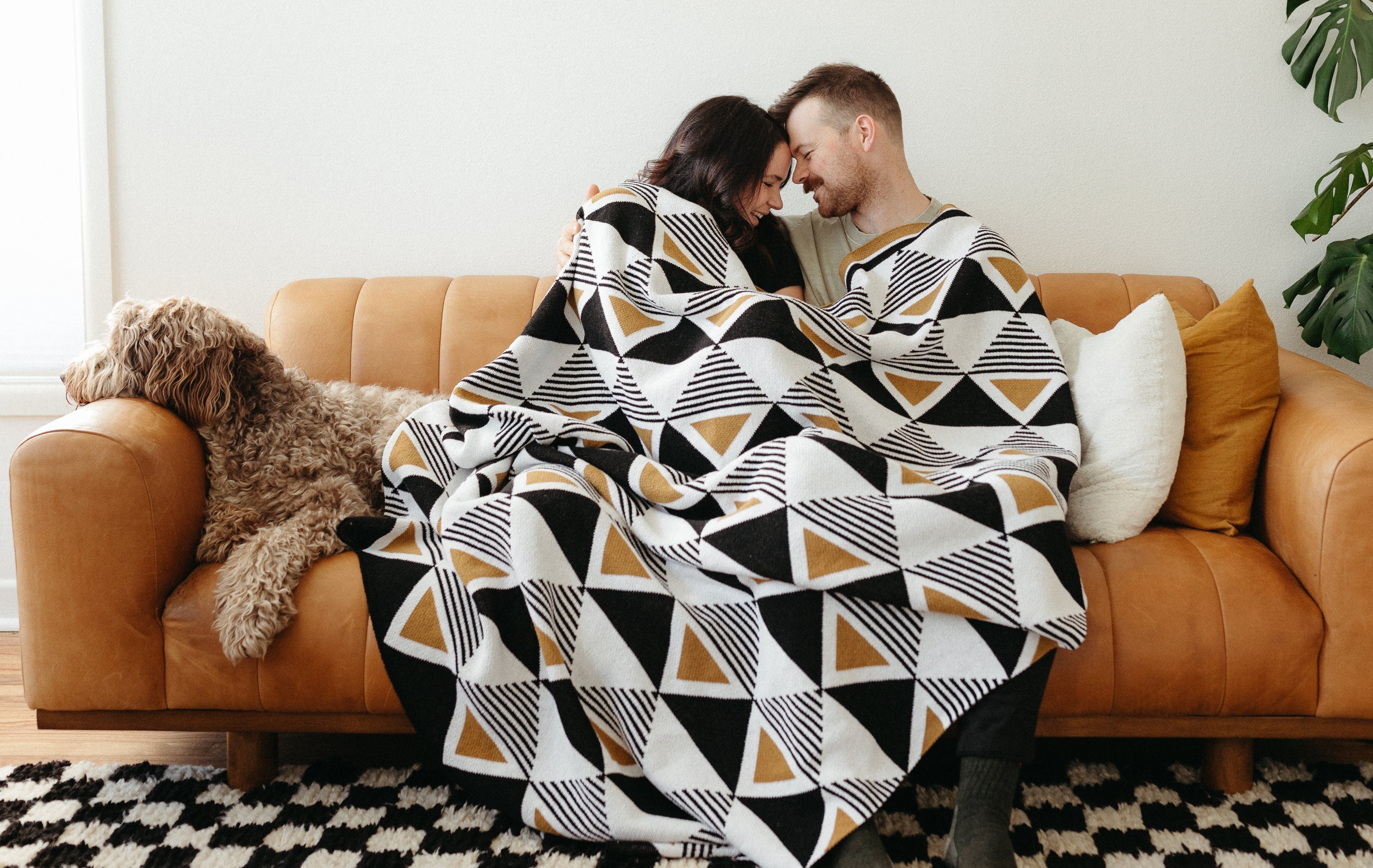 a cute couple cuddled up on a leather couch under a Seek & Swoon Envie Throw with their dog